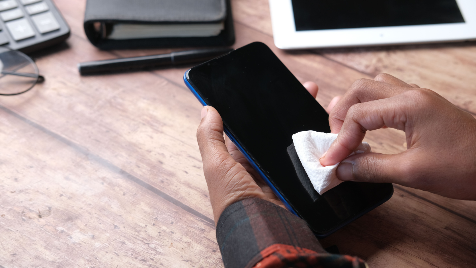Pessoa secando um celular com pano de microfibra após contato com água.