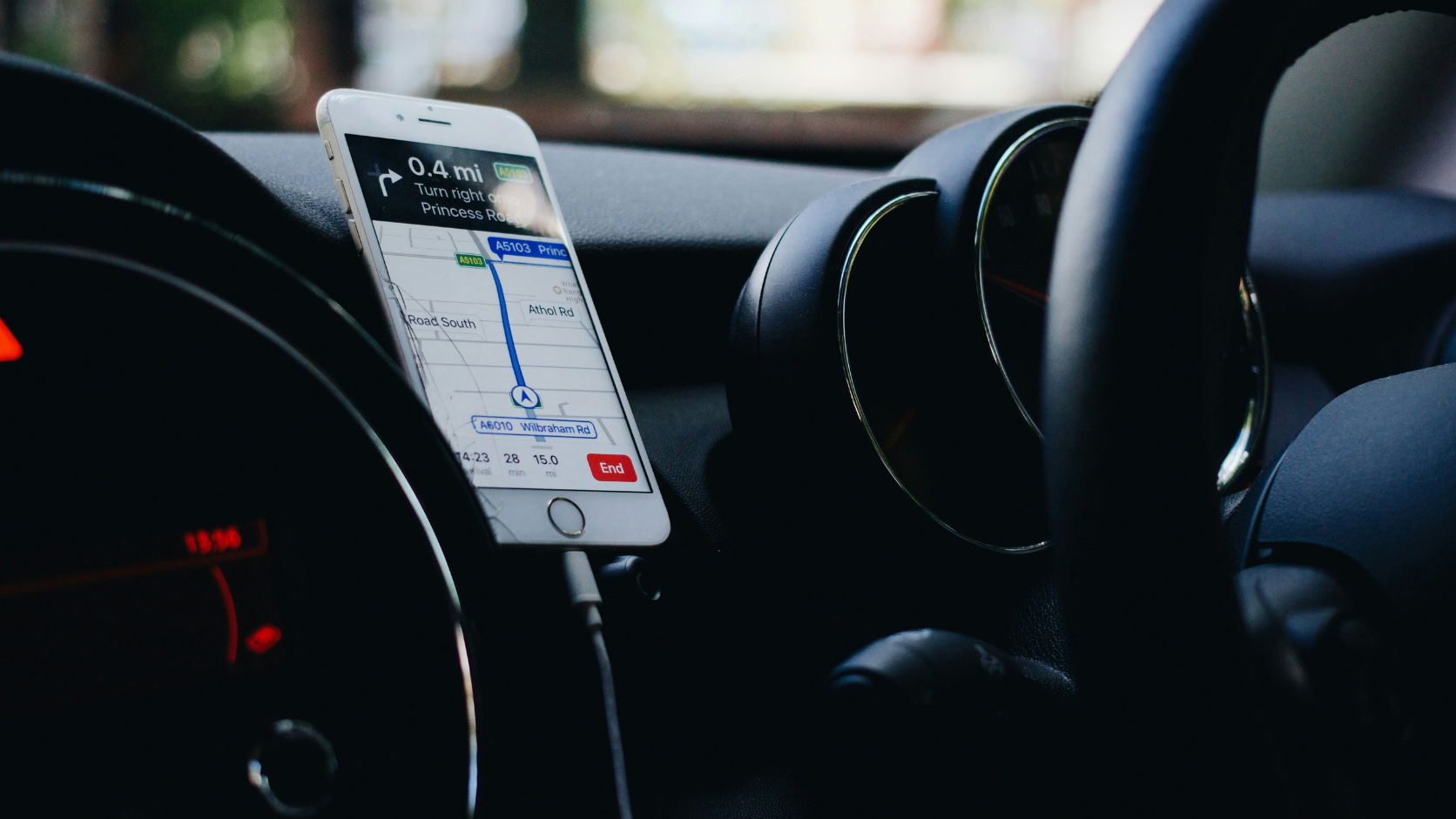Smartphone fixado em suporte no painel do veículo mostrando aplicativo de navegação GPS conectado via cabo.