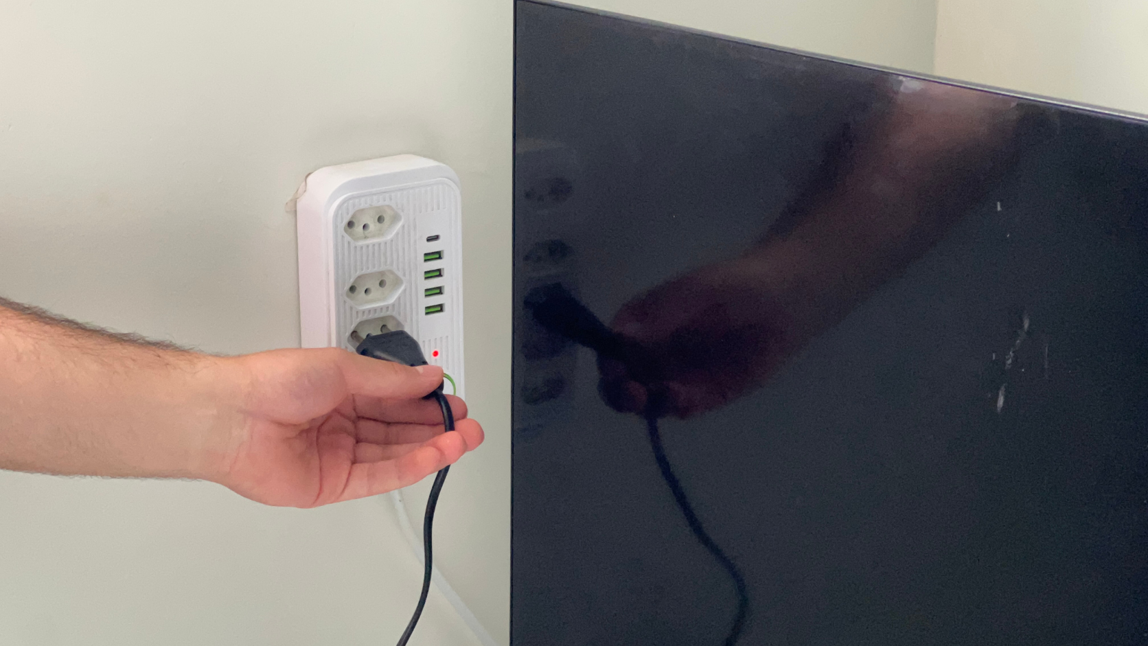 Mão desconectando o cabo de energia da Smart TV da tomada de parede