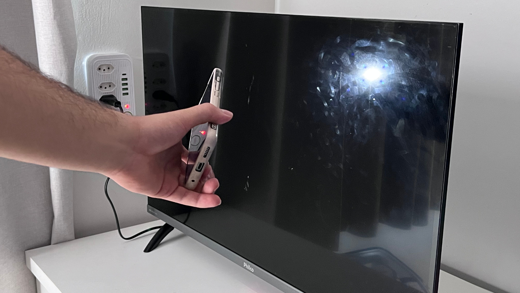 Lanterna do celular apontada bem de perto para a tela preta da TV no escuro